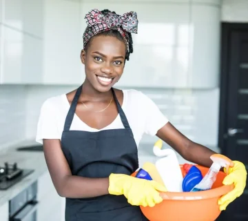 عاملة منزلية تبتسم أثناء أداء مهام التنظيف في منزل سعودي، ترتدي زي العمل الرسمي